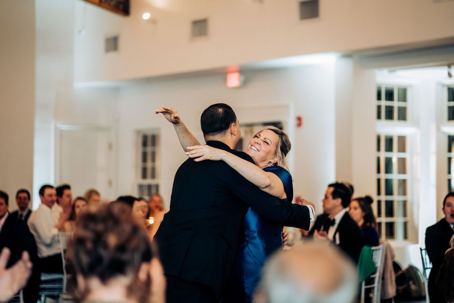 A formal dance at an elegant venue with exposed wood beams and white walls as guests watch from their tables.