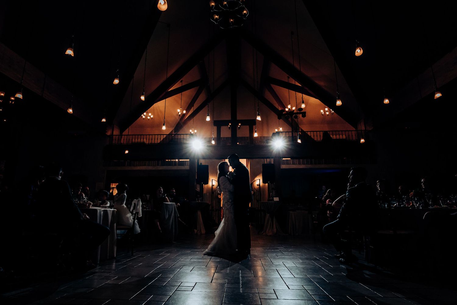 A silhouetted couple dances in an elegant venue with dramatic lighting and vaulted ceilings.