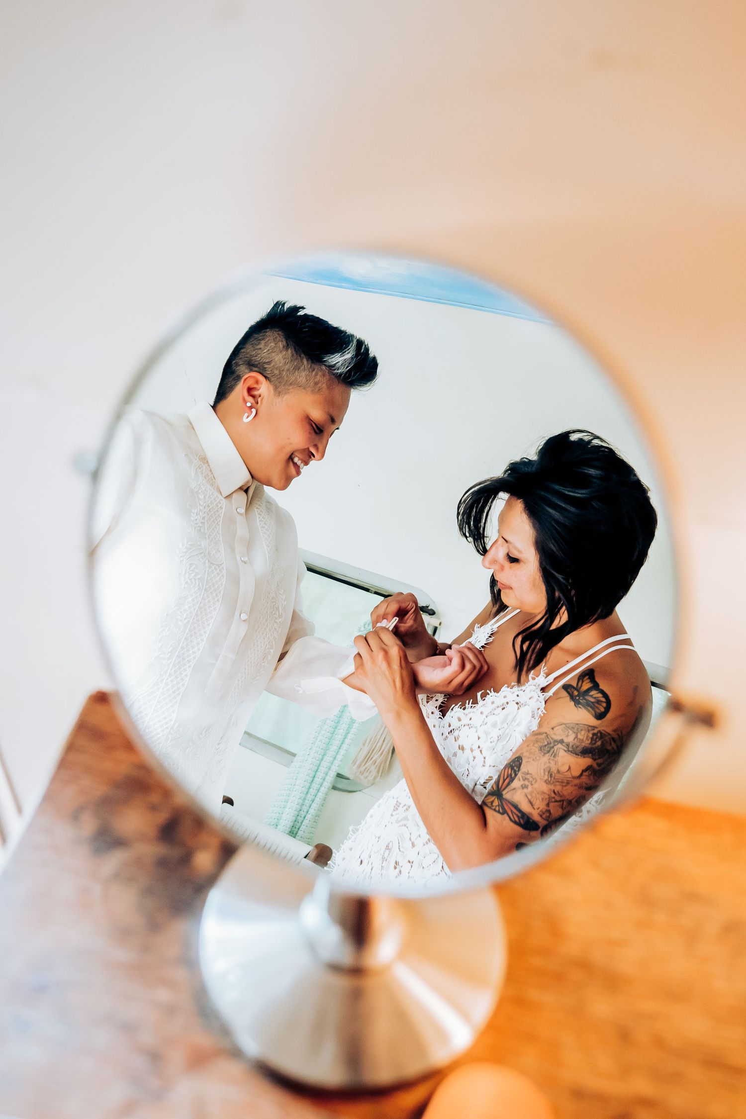 Reflection in a circular mirror showing two people doing makeup together.