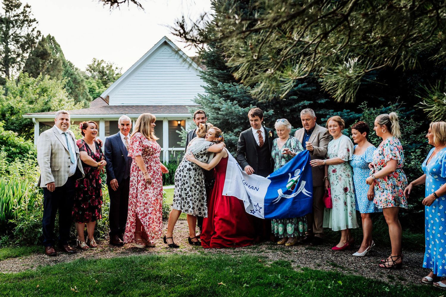 Wedding guests gather on a lawn in colorful dresses in front of a white gazebo.