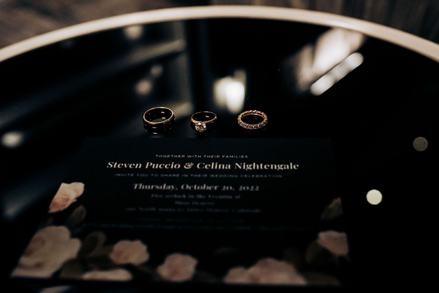 Wedding rings arranged artistically on a black reflective surface with names visible.