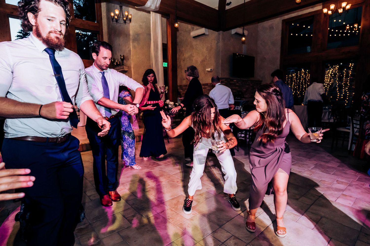 Guests dance energetically on a dimly lit dance floor at a wedding reception.