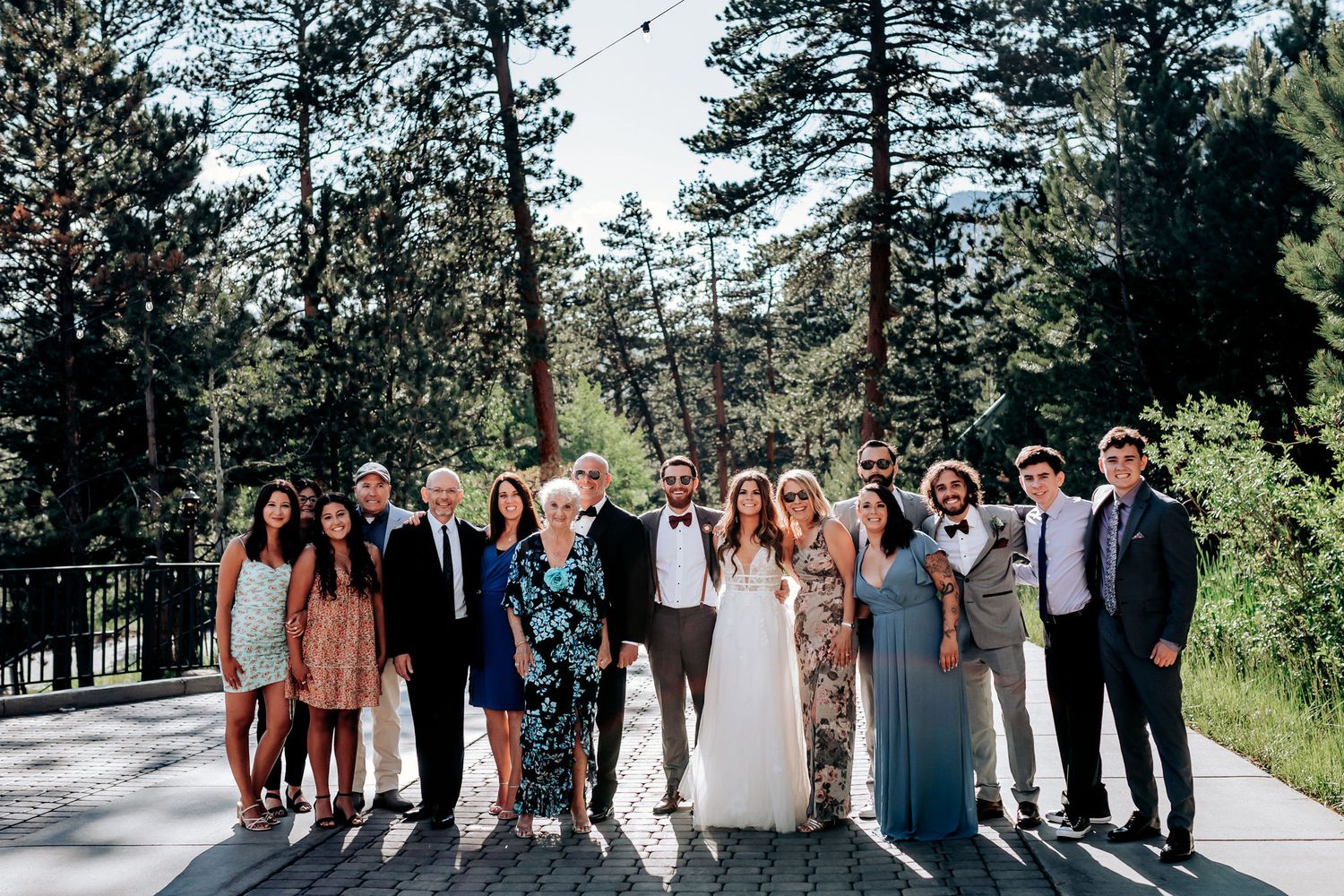 Wedding party poses together on stone pathway surrounded by evergreen trees.