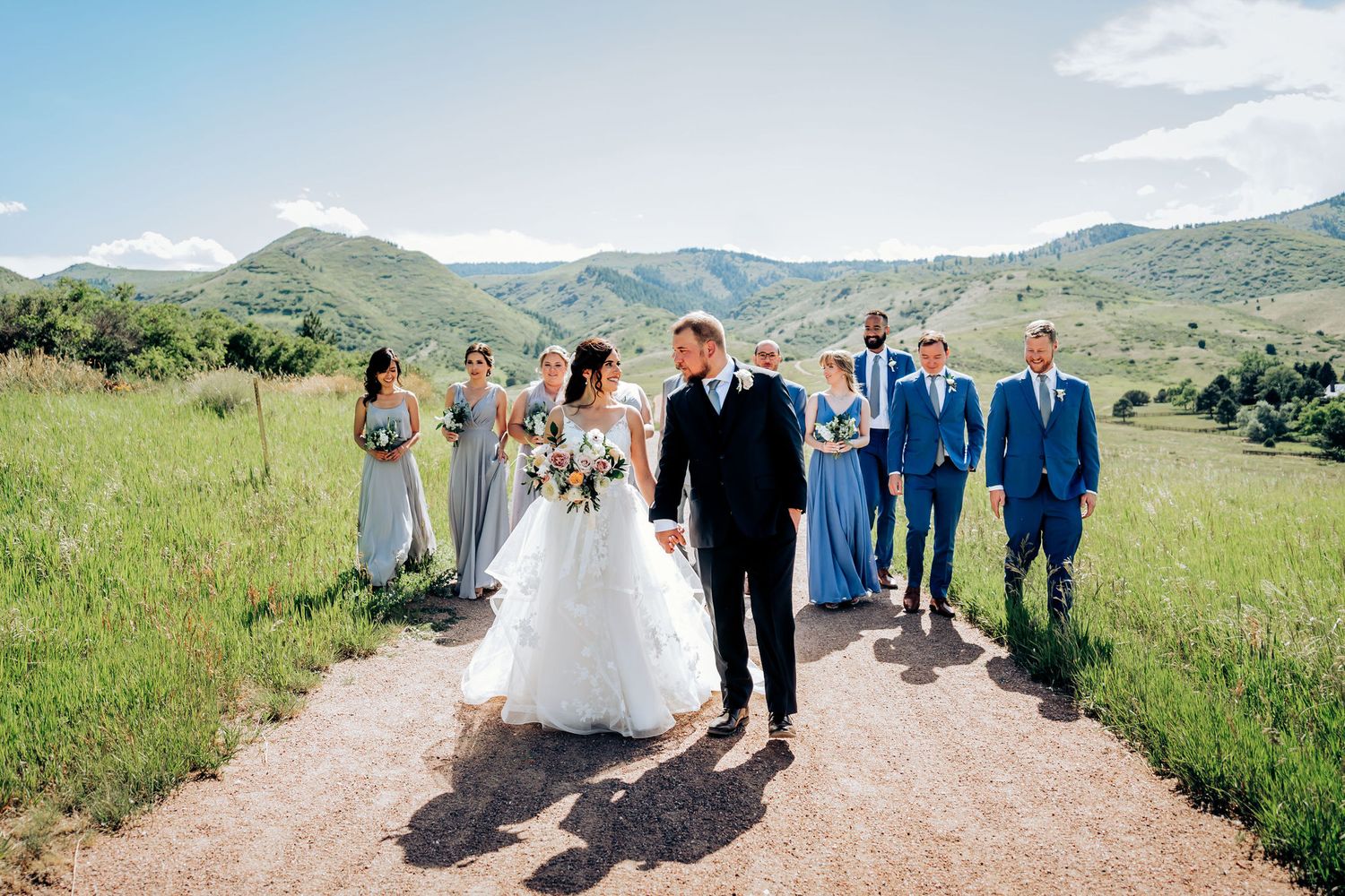Wedding party walking down a dirt path with scenic mountain views in the background.