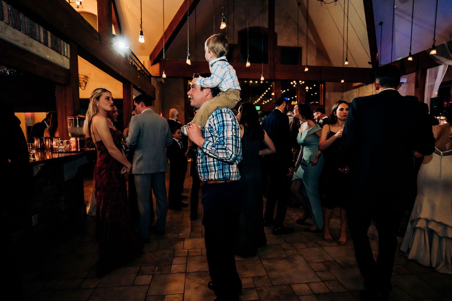 Wedding reception guests dancing and enjoying themselves in a dimly lit venue.