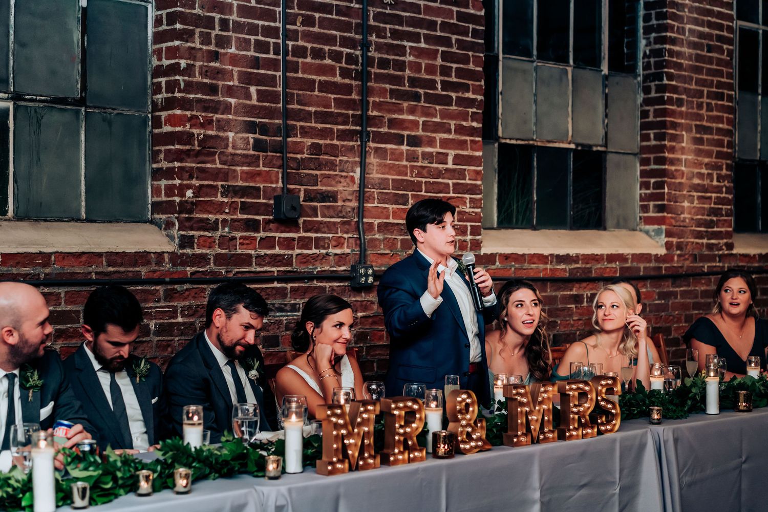 Wedding party seated at head table with Mr and Mrs marquee letters during reception in brick venue.