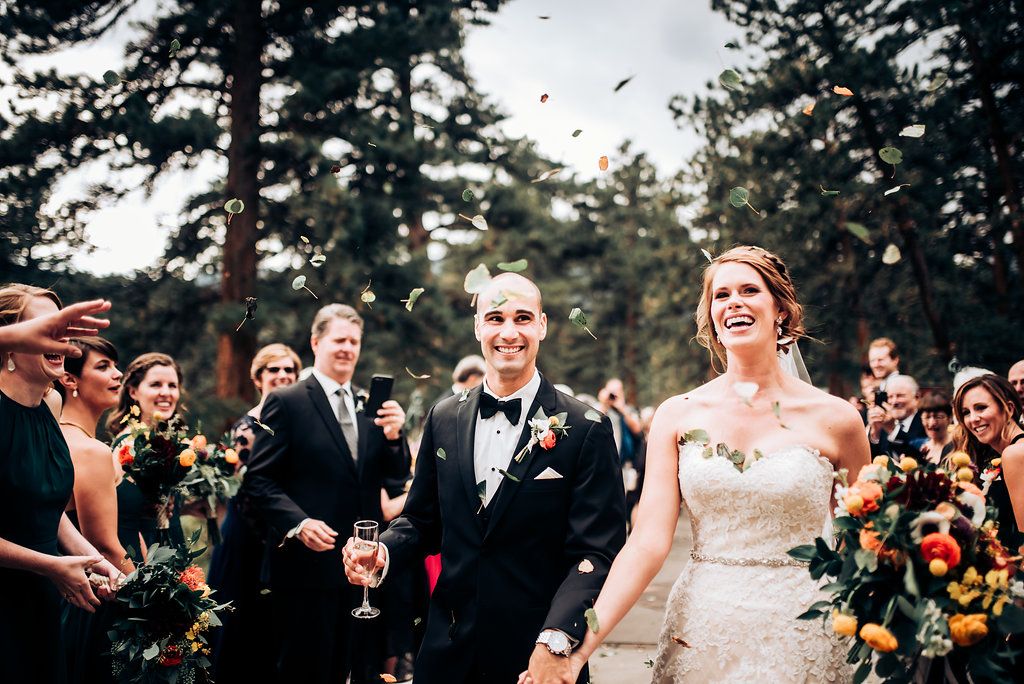 Joyful outdoor wedding celebration with guests throwing confetti among tall pine trees.