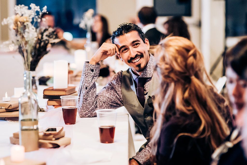Wedding reception dinner with guests enjoying conversation at decorated tables.