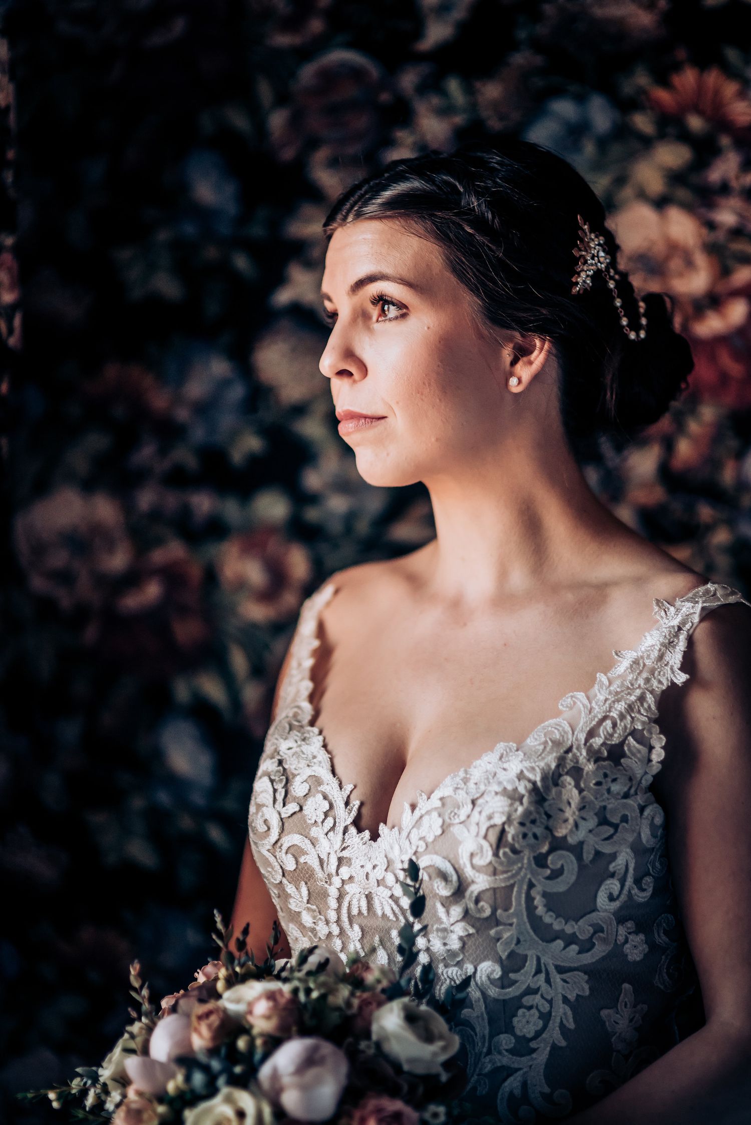 Artistic bridal portrait against dark floral wallpaper with soft natural light.