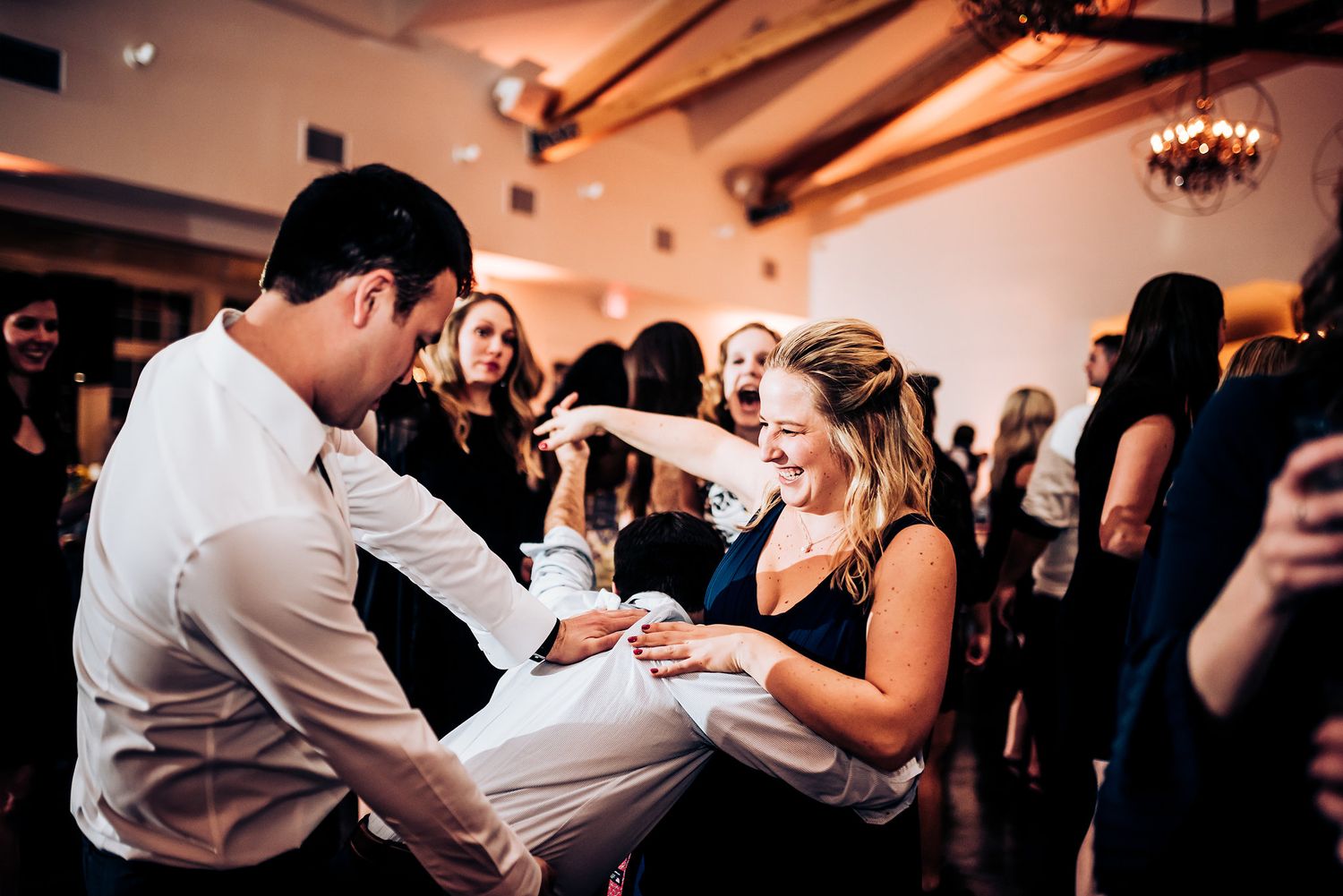 Wedding guests celebrate on dance floor during reception festivities.