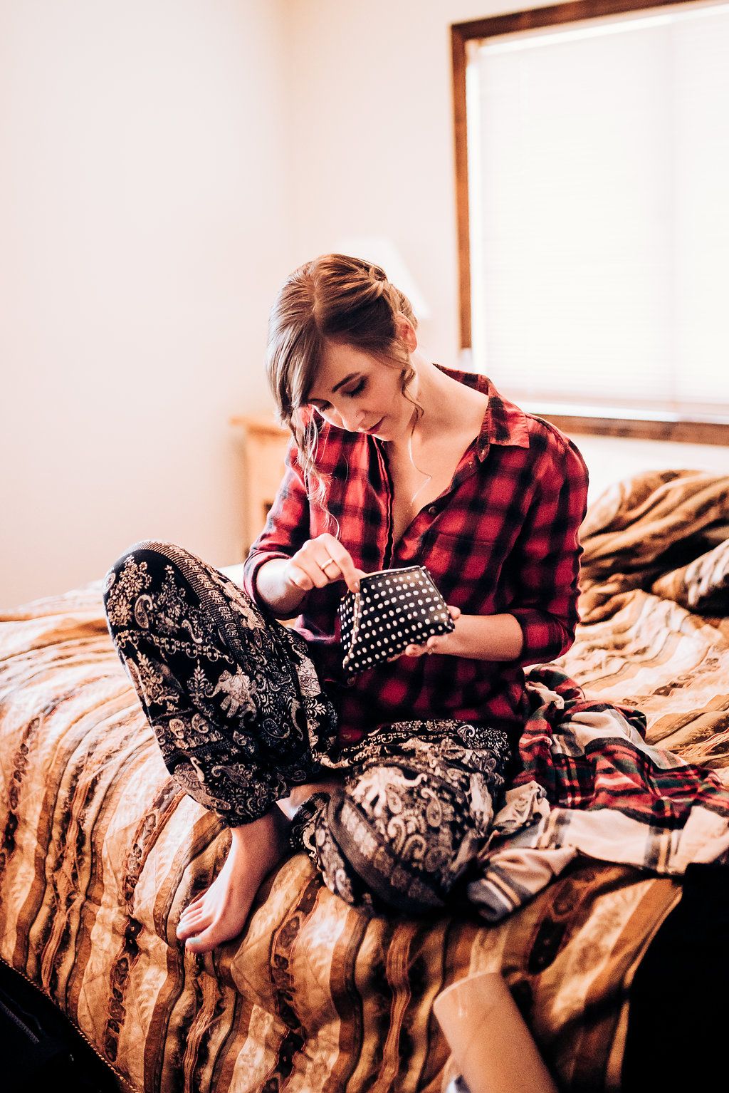 Someone in a red plaid shirt sits cross-legged on a bed while using a laptop.