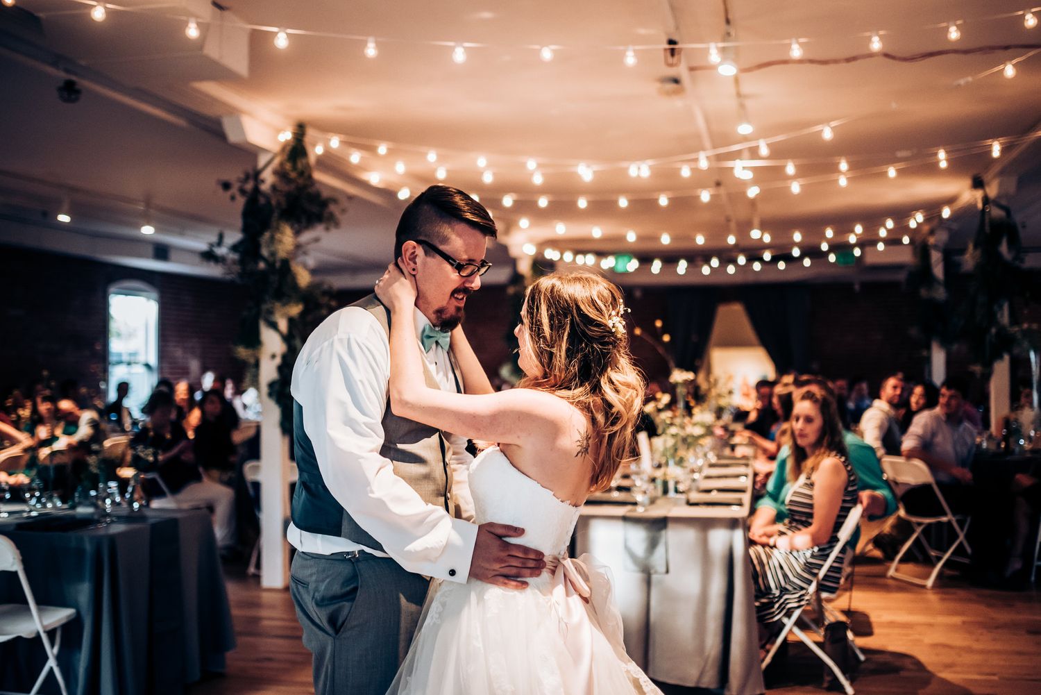 Couple dancing under string lights at an indoor wedding reception venue.