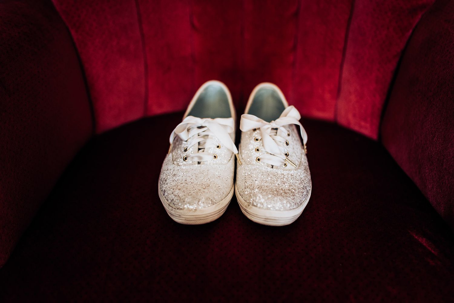 White glittery sneakers displayed on a red velvet chair.