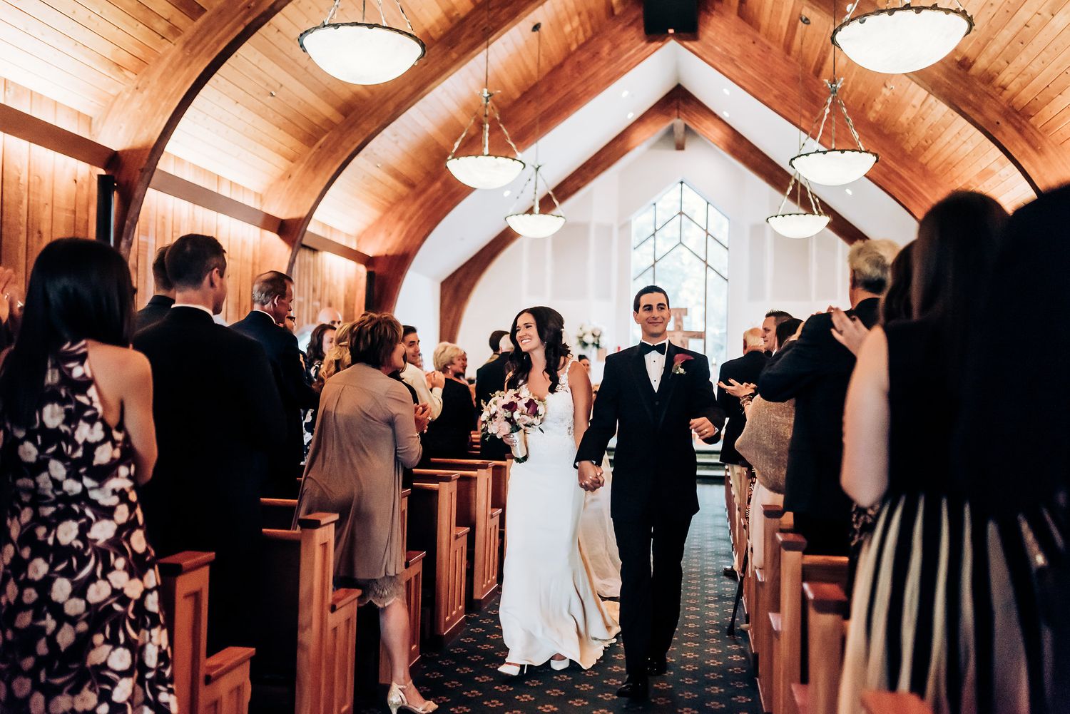 Wedding couple exits down church aisle while guests line the pews.