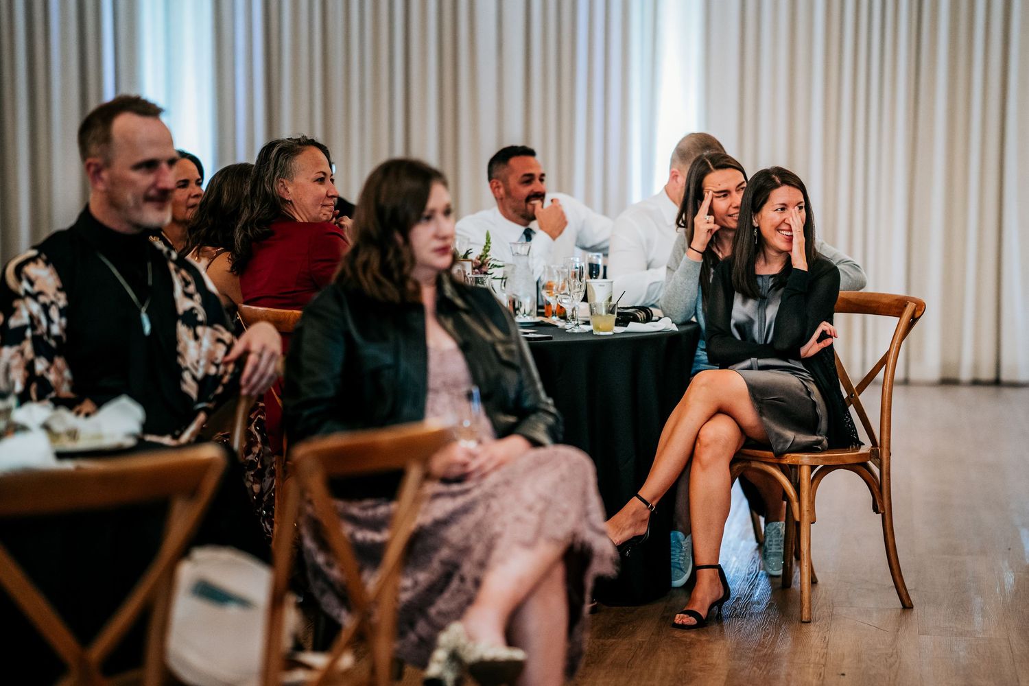 Wedding reception guests laugh and smile during heartfelt speeches at indoor venue.