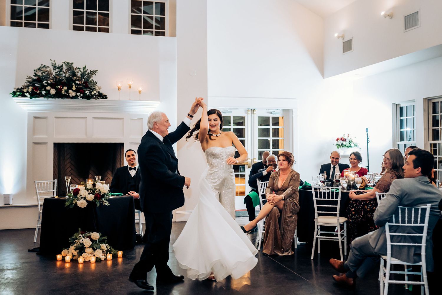 Dancing couple twirls on the dance floor while guests watch from their seats in an elegant white venue.