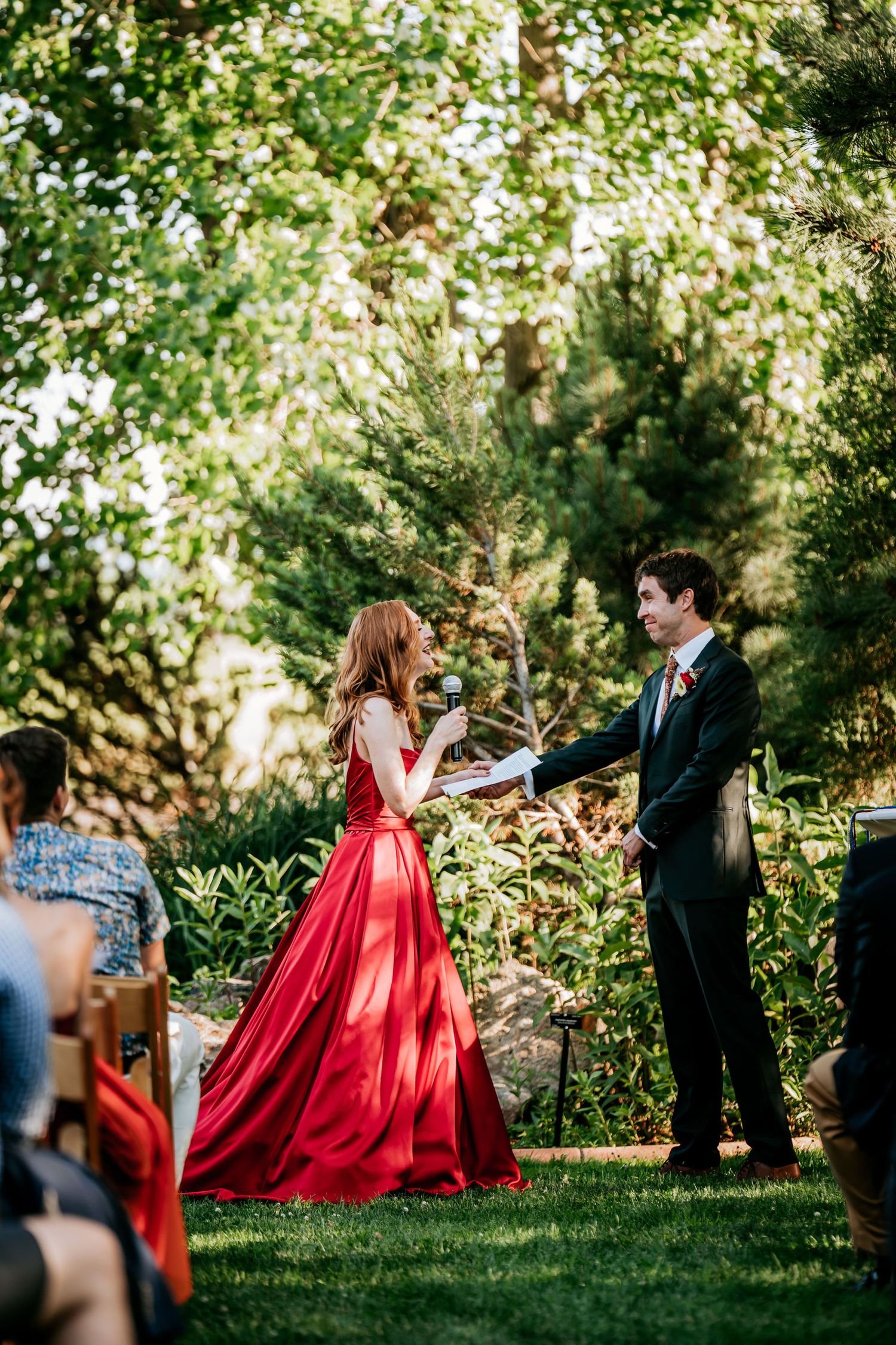 A couple participates in a garden ceremony with the person in red holding flowers.