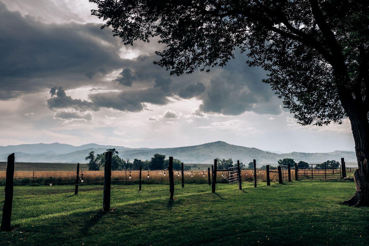 Dramatic mountain landscape at sunset with fenced pasture in foreground.
