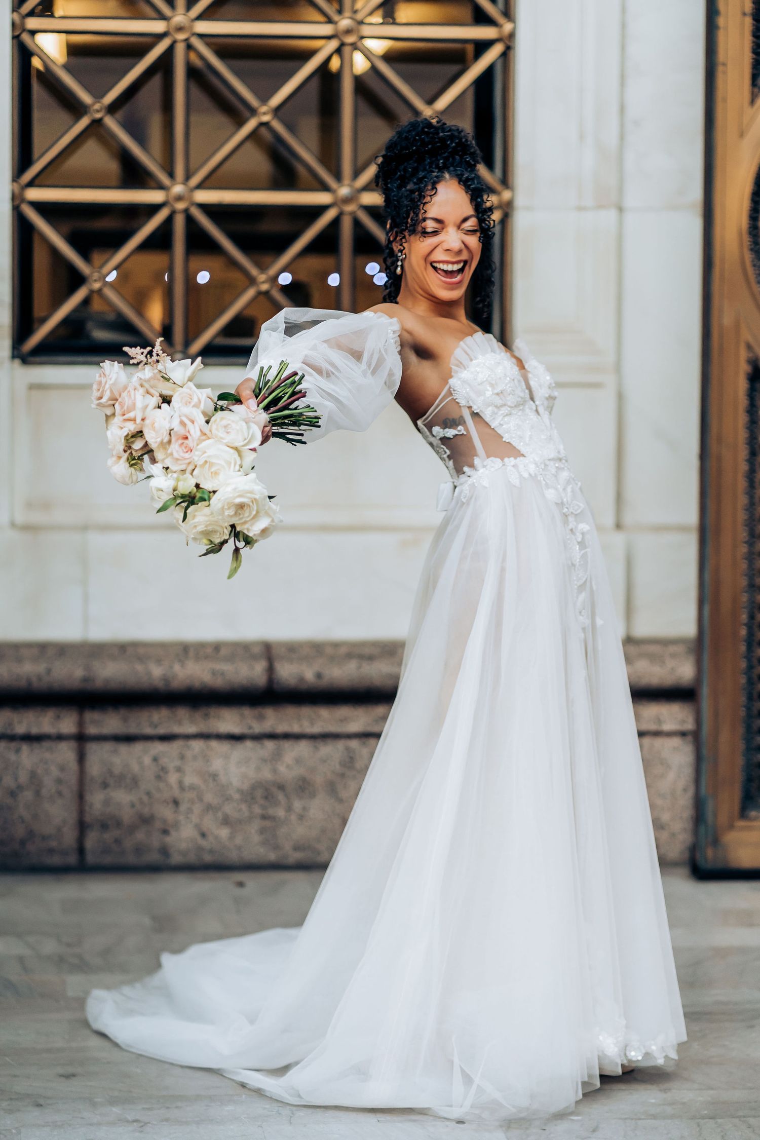 Elegant bridal portrait with white floral bouquet against architectural background.