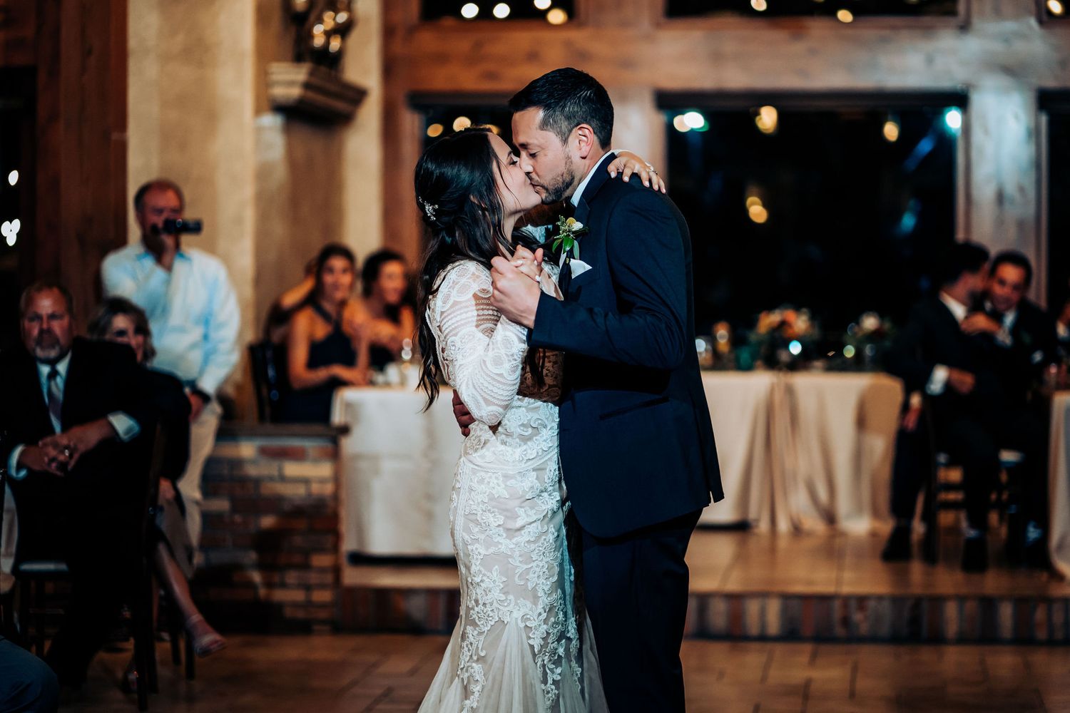 Intimate slow dance moment during a wedding reception with ambient lighting and guests looking on.