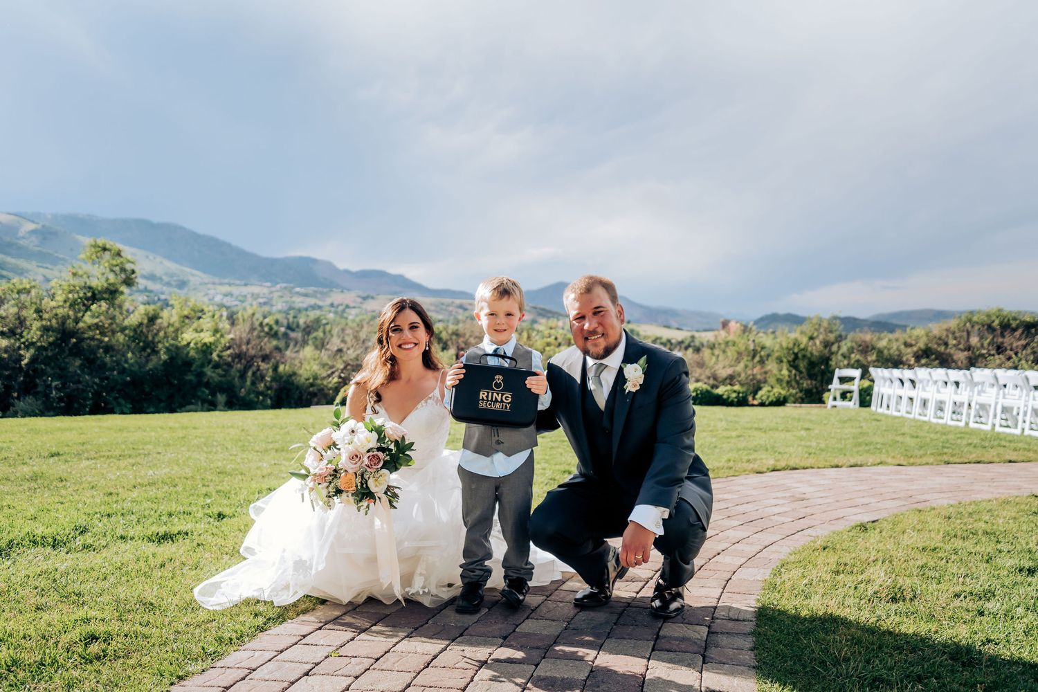 Wedding portrait on brick path with mountain scenery and white ceremony chairs visible.