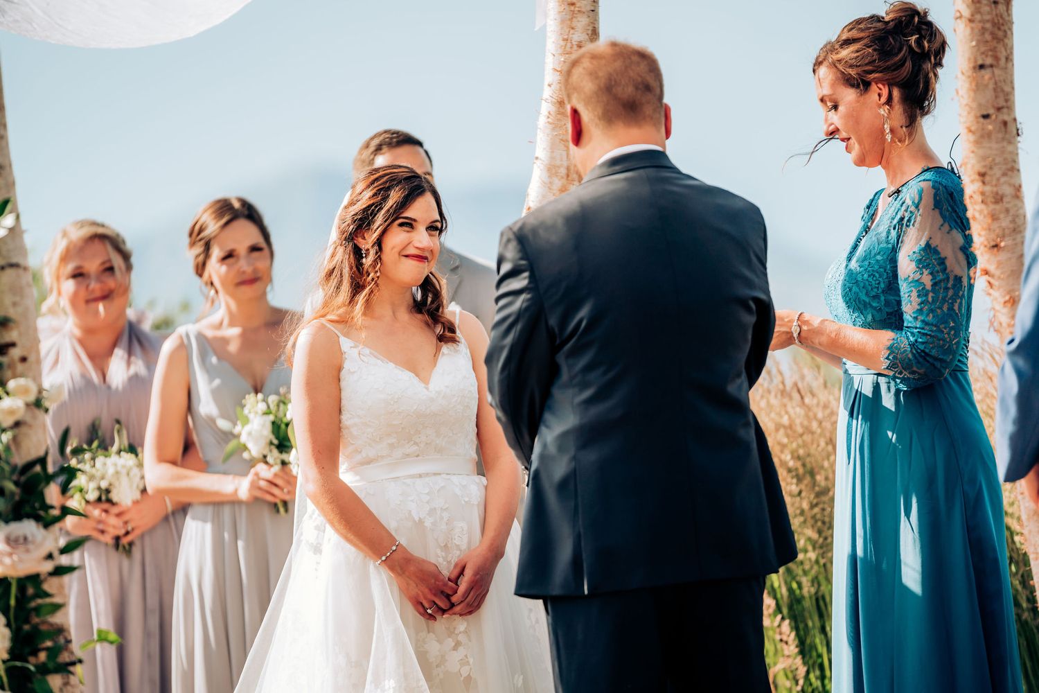 Wedding ceremony under decorated wooden arch with mountain landscape in background.