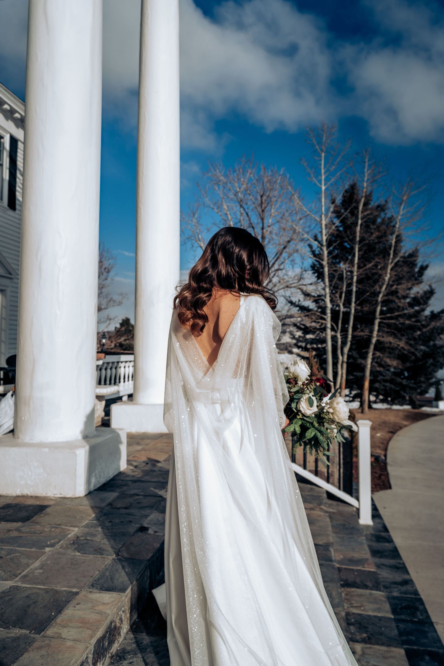 Ethereal bridal portrait showing a flowing white dress and veil against classic white columns.