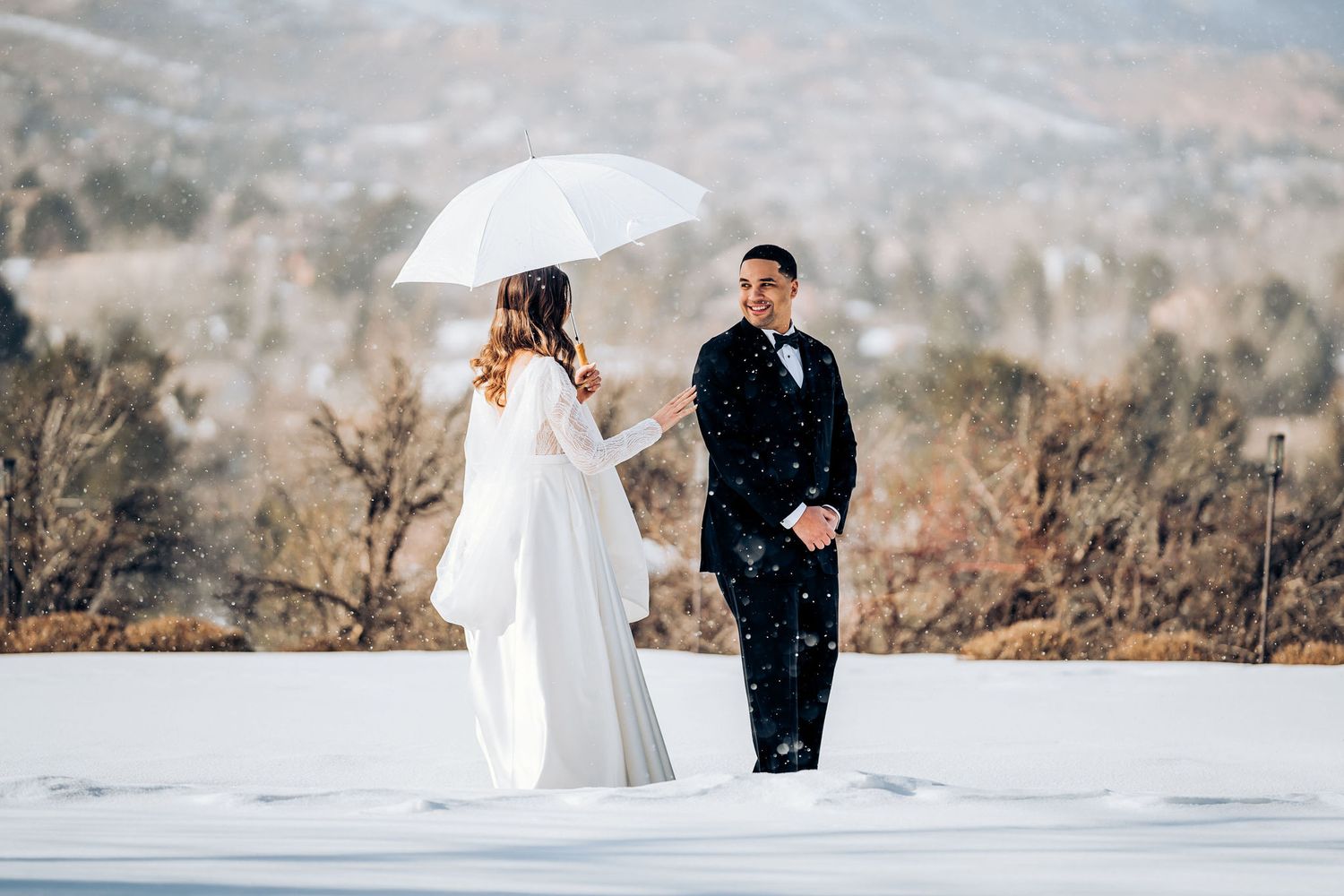 A winter wedding photoshoot with a white umbrella against a snowy mountain landscape.