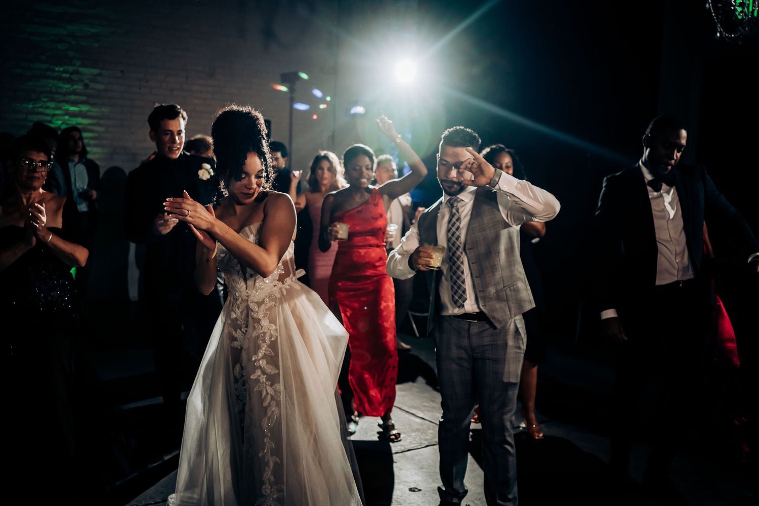 Wedding guests dance in formation at a lively reception with dramatic lighting effects.