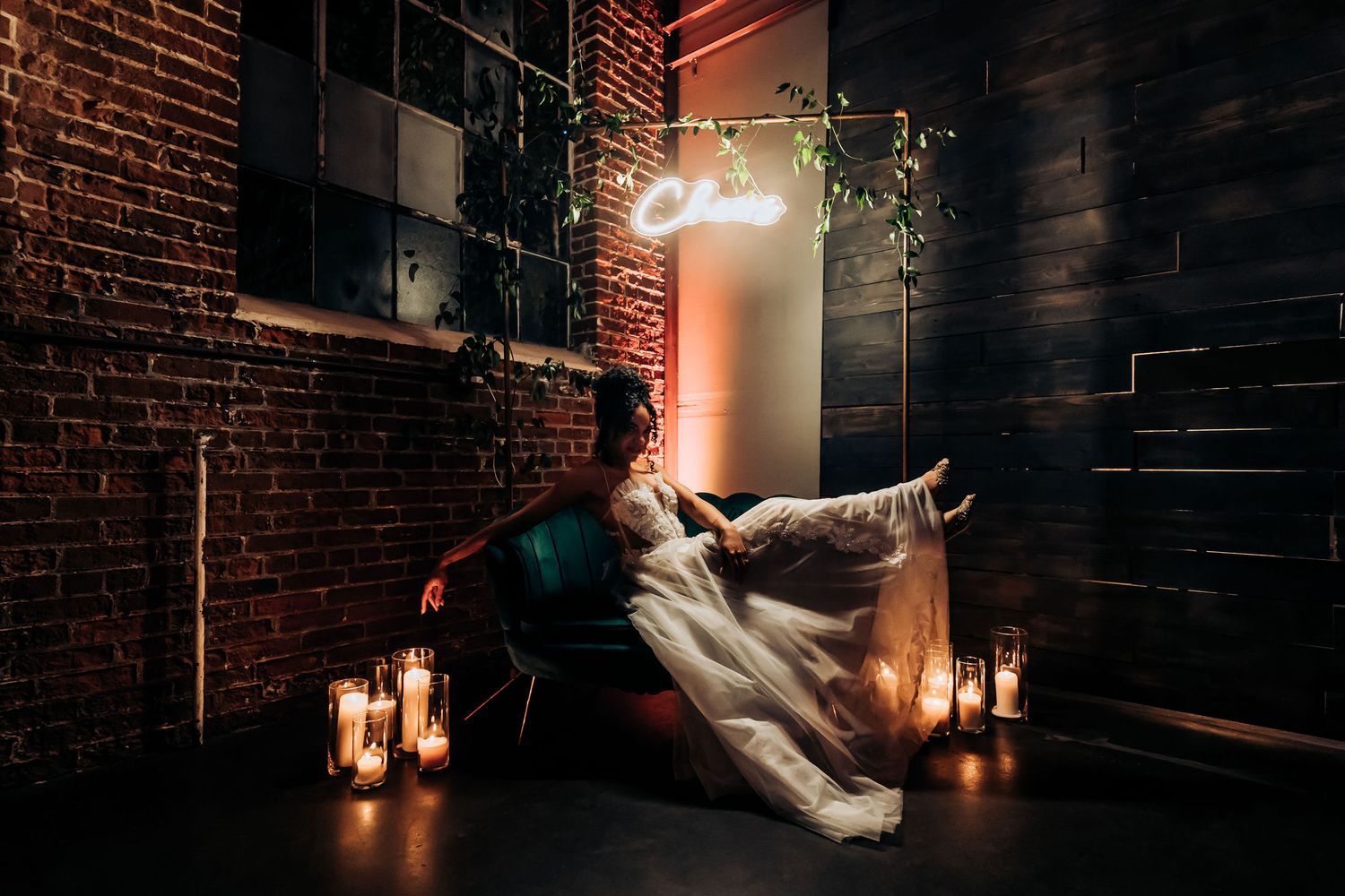 Artistic wedding portrait with couple against brick wall surrounded by candles and soft lighting.