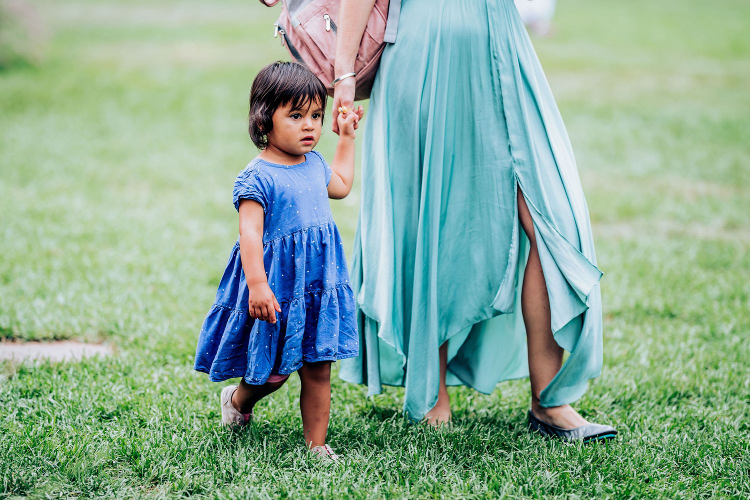 Adult and child in blue and mint dresses hold hands while walking on grass.