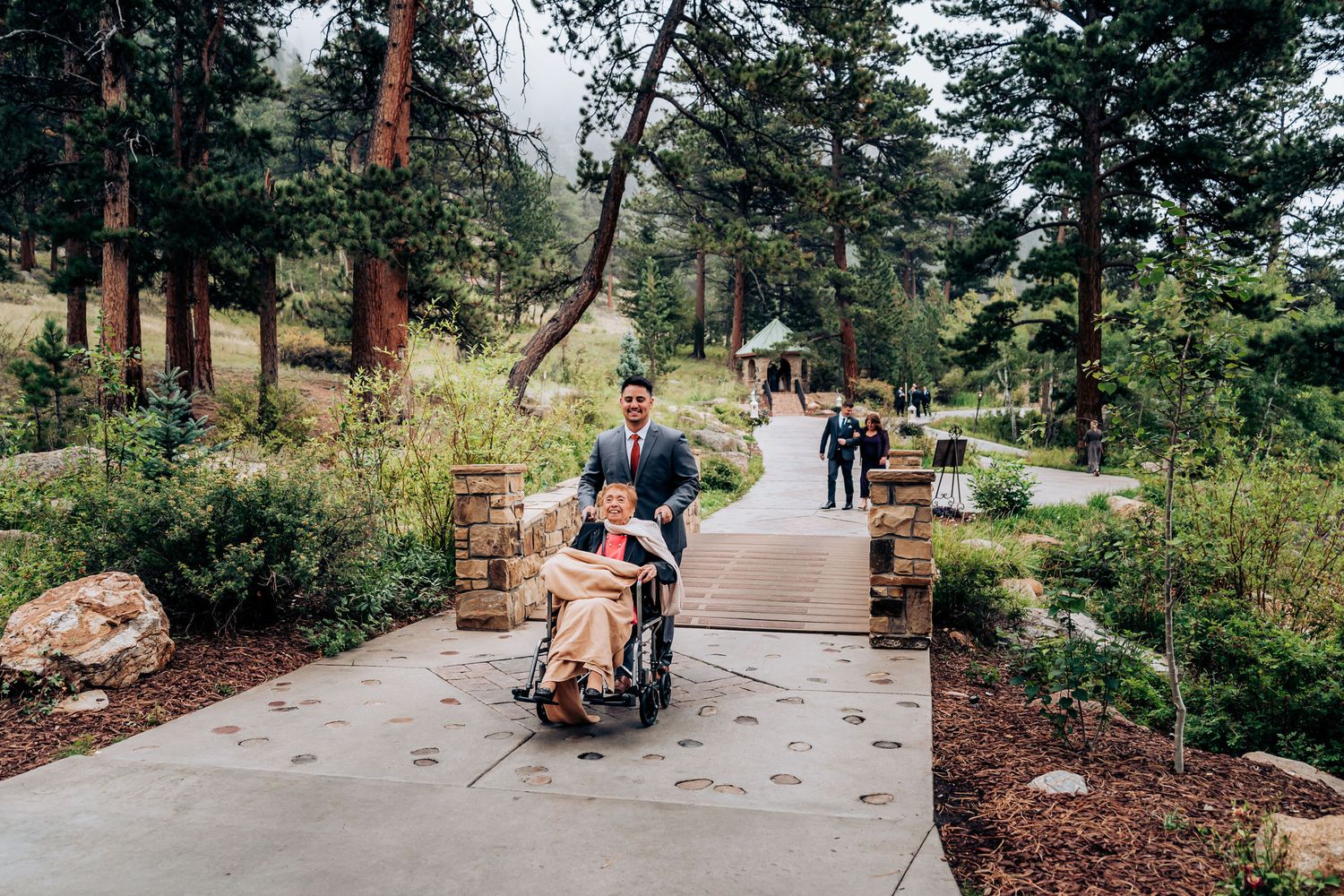 Wedding party walking on concrete pathway through mountain forest setting.