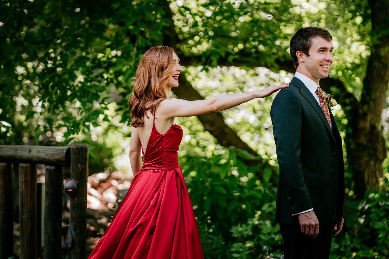 Playful formal portrait session in lush green garden setting with red gown and dark suit.