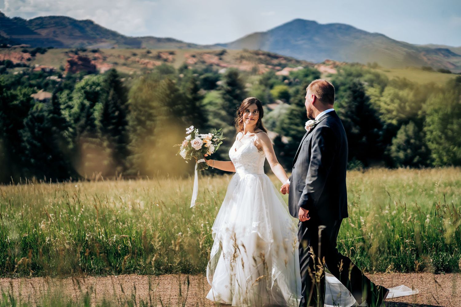 Bride and groom pose together in front of mountain landscape holding wedding bouquet.