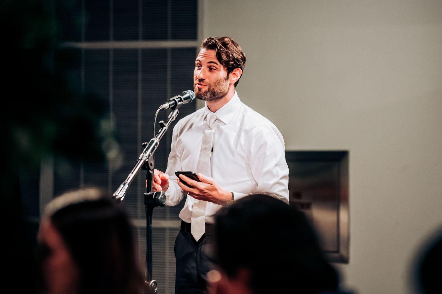 Speaker addressing wedding guests at reception with microphone in hand.