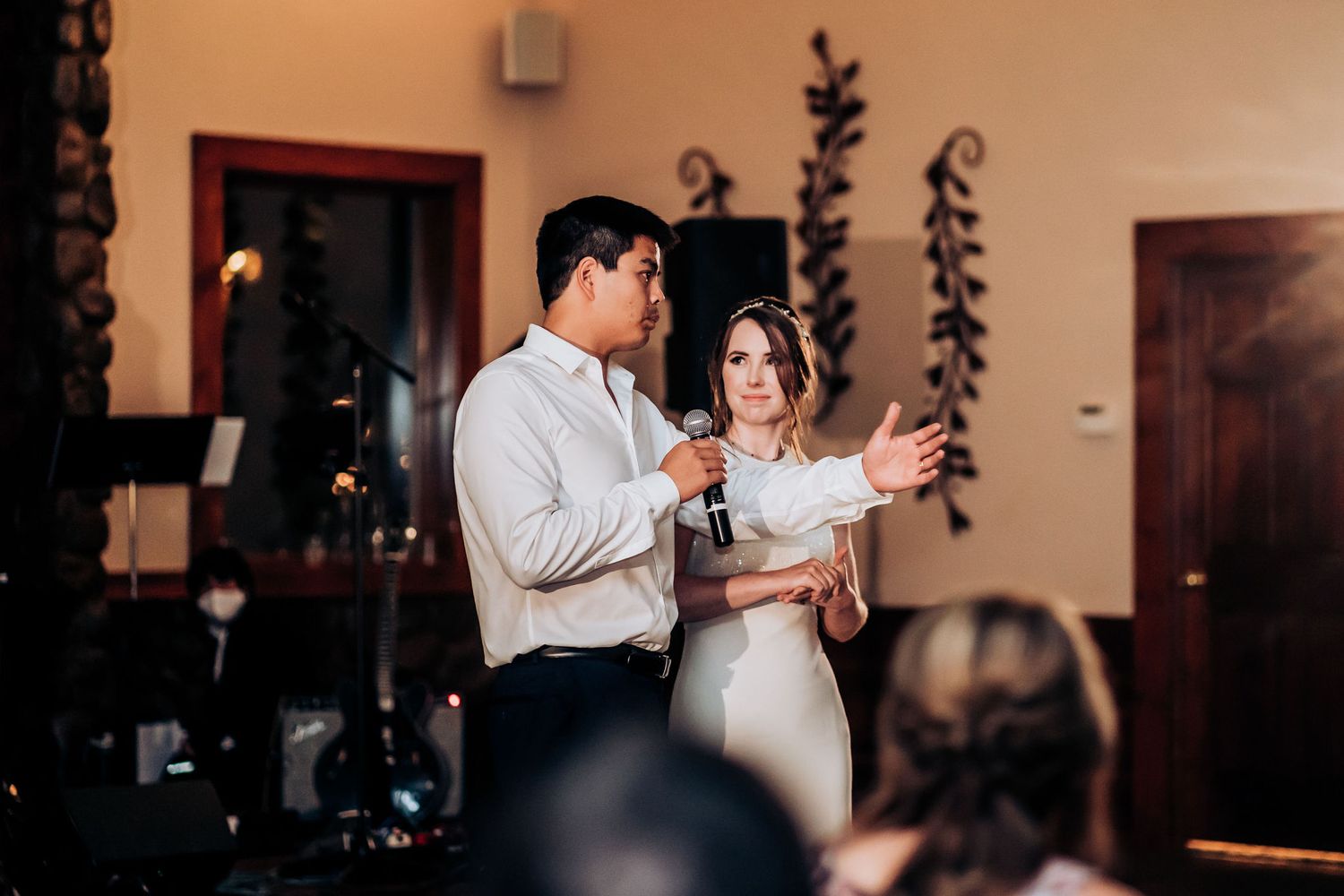 Wedding speech moment captured during evening reception with decorative vine wall accents.