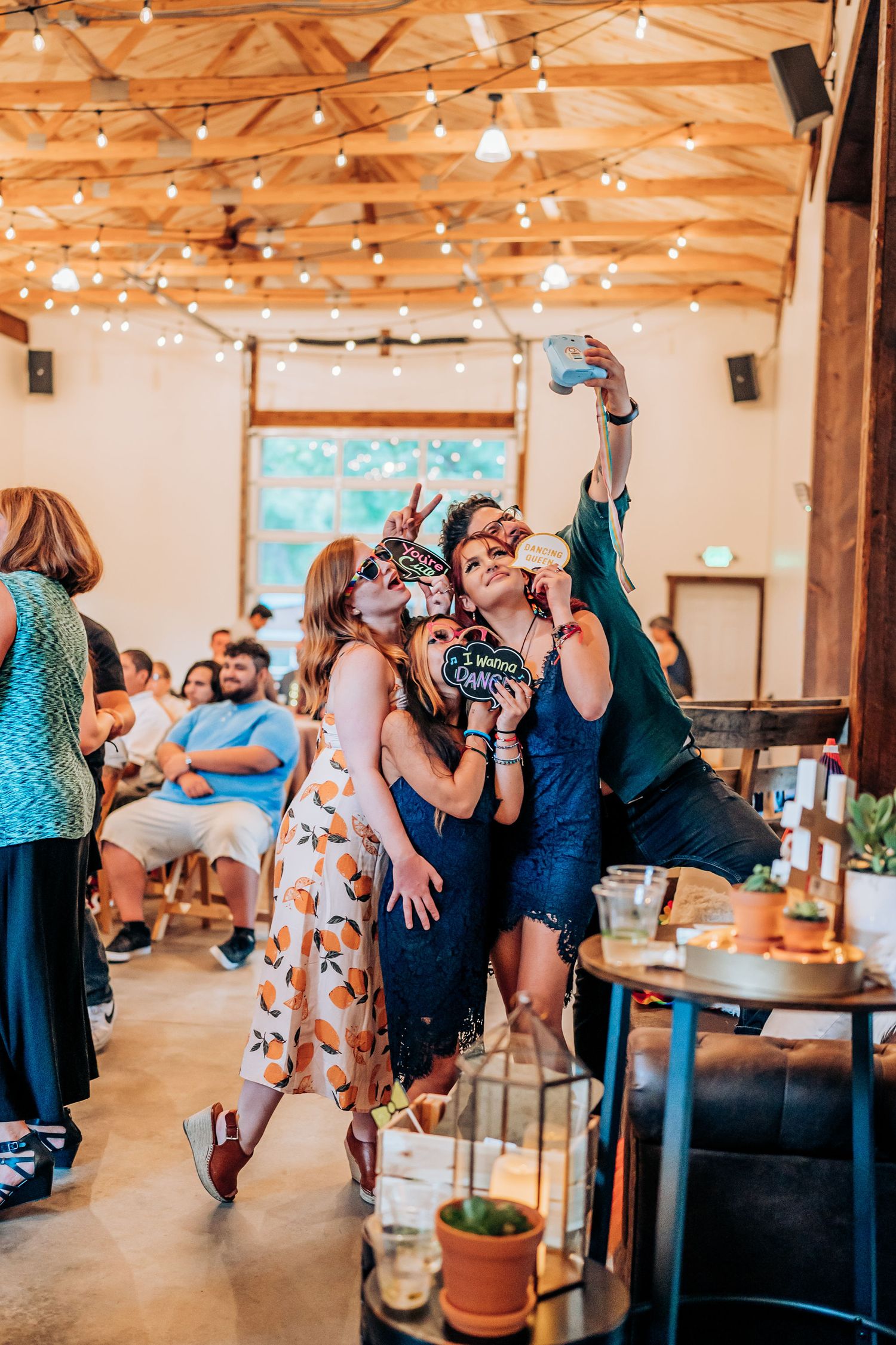 Wedding reception celebration with string lights and guests taking group selfies in rustic venue.