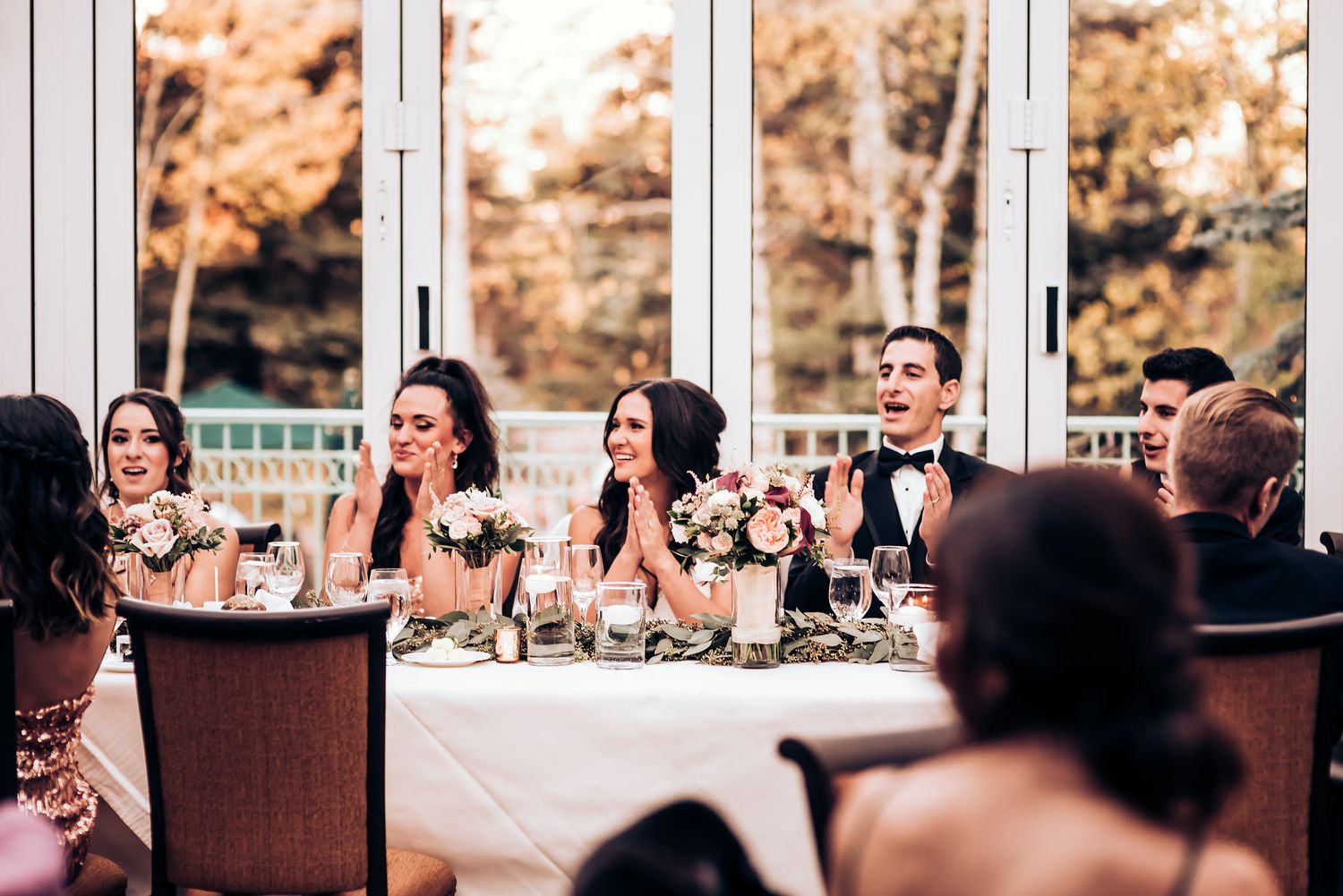Wedding guests react emotionally during reception speeches at an elegant dining table with wine glasses.