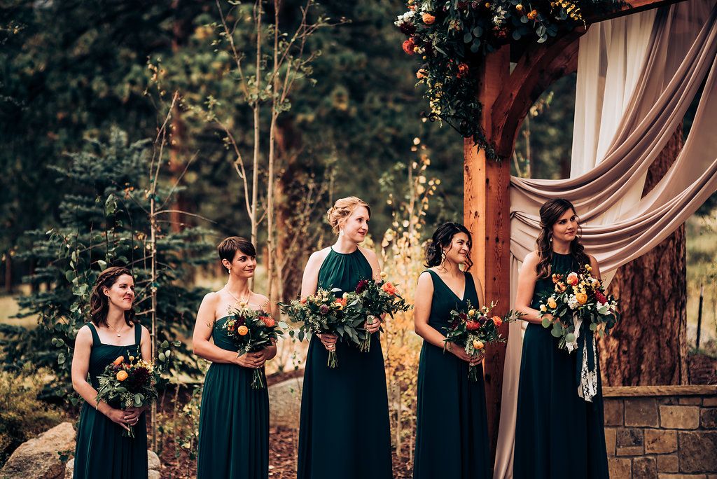 Bridesmaids in navy dresses stand elegantly holding bouquets during outdoor ceremony.