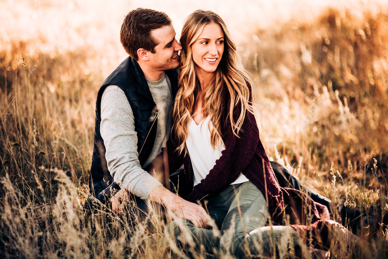 A couple relaxes together in a sunlit meadow with golden grasses during an autumn afternoon.