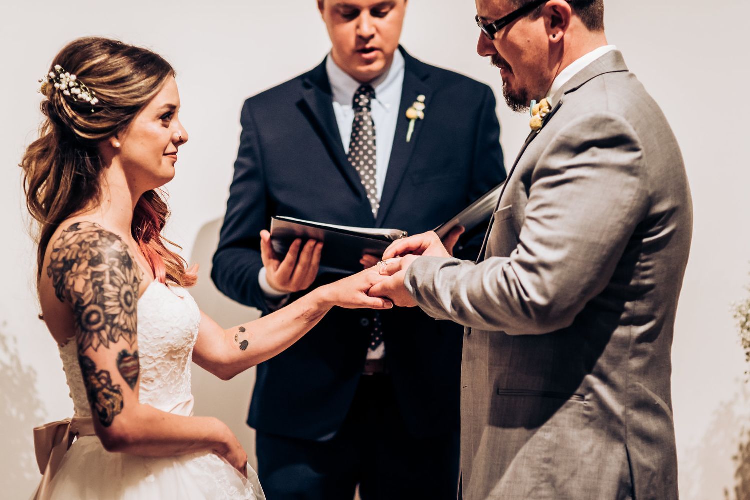 Ring exchange moment during wedding ceremony in front of modern artwork.