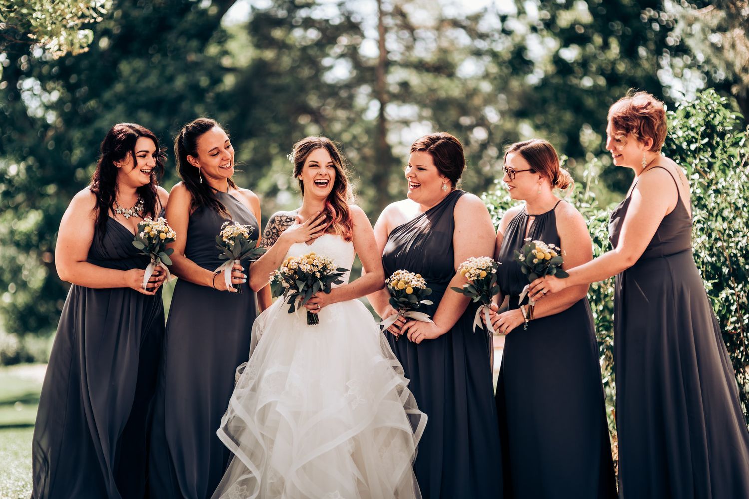 Bridesmaids in navy dresses laugh with bride during outdoor wedding celebration.