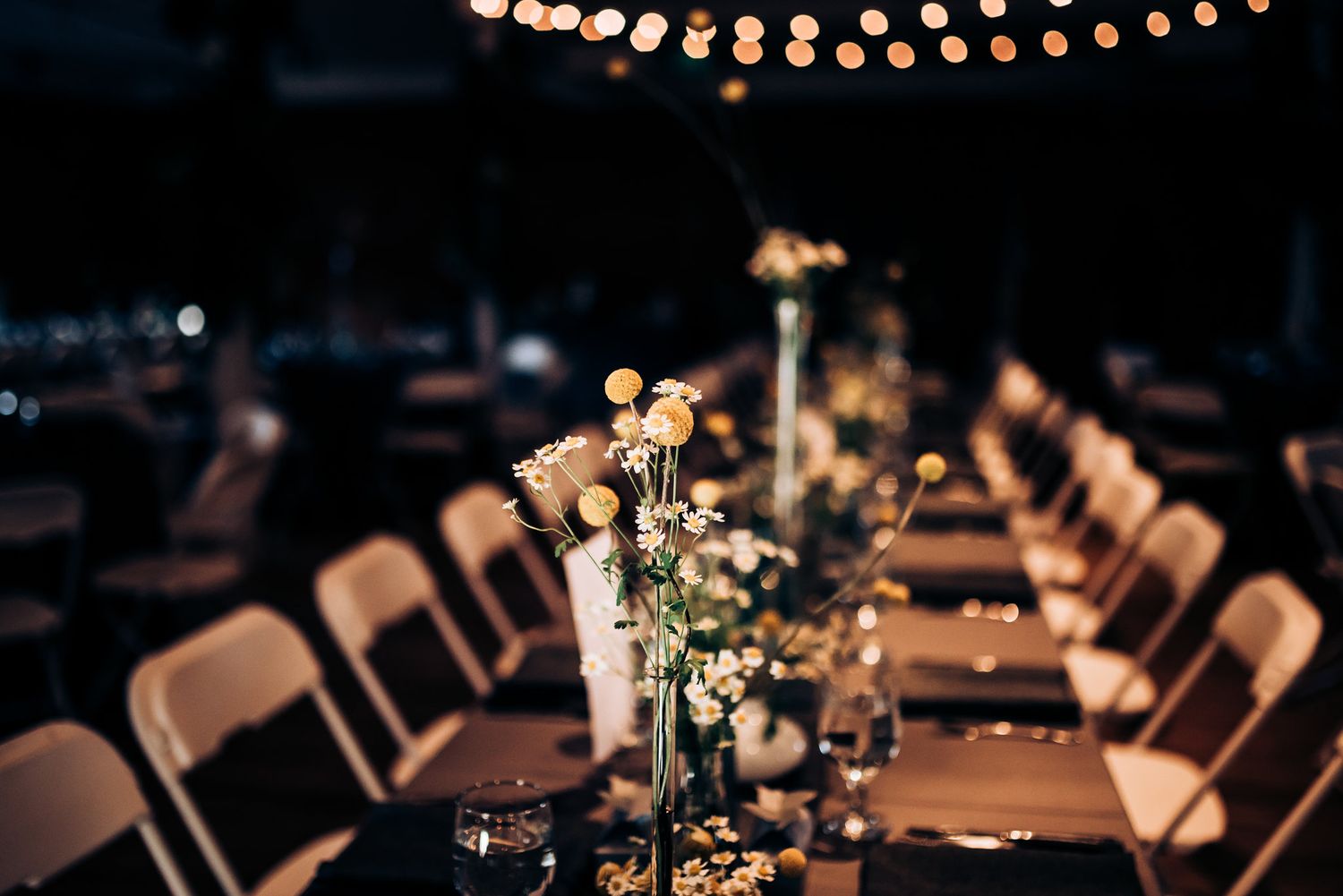 Wedding reception tables set with floral centerpieces under warm string lights.