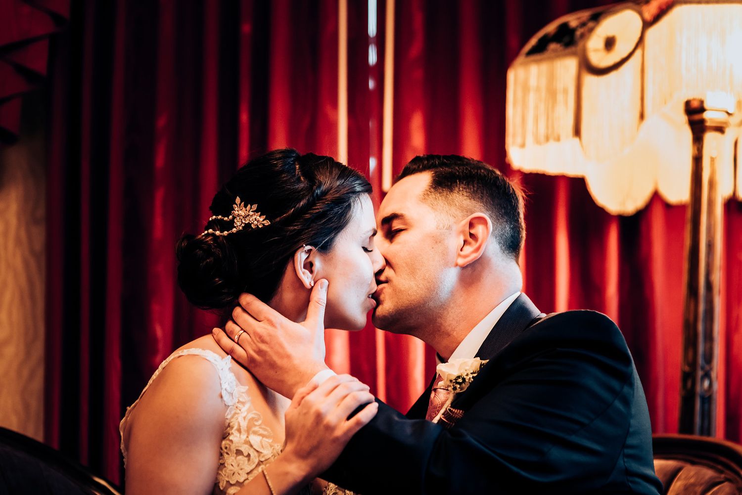 Intimate wedding moment captured against red velvet curtain backdrop.