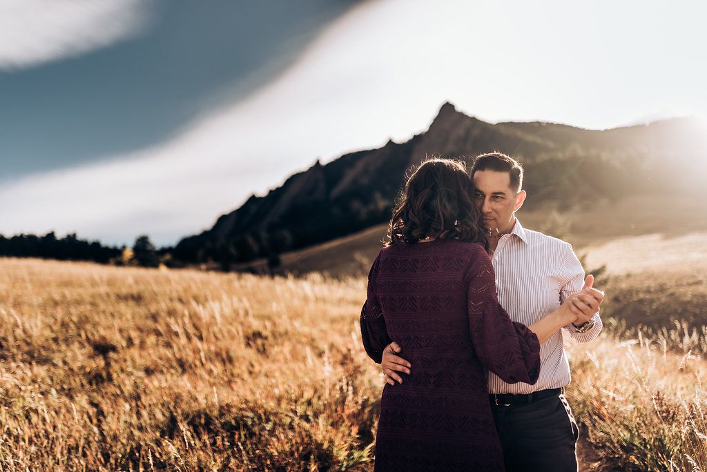 Couple embracing in golden mountain field during sunset.