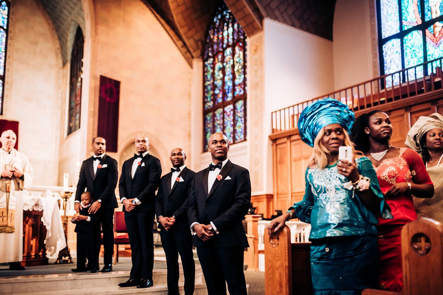 Wedding ceremony in church with stained glass windows and formal wedding party.