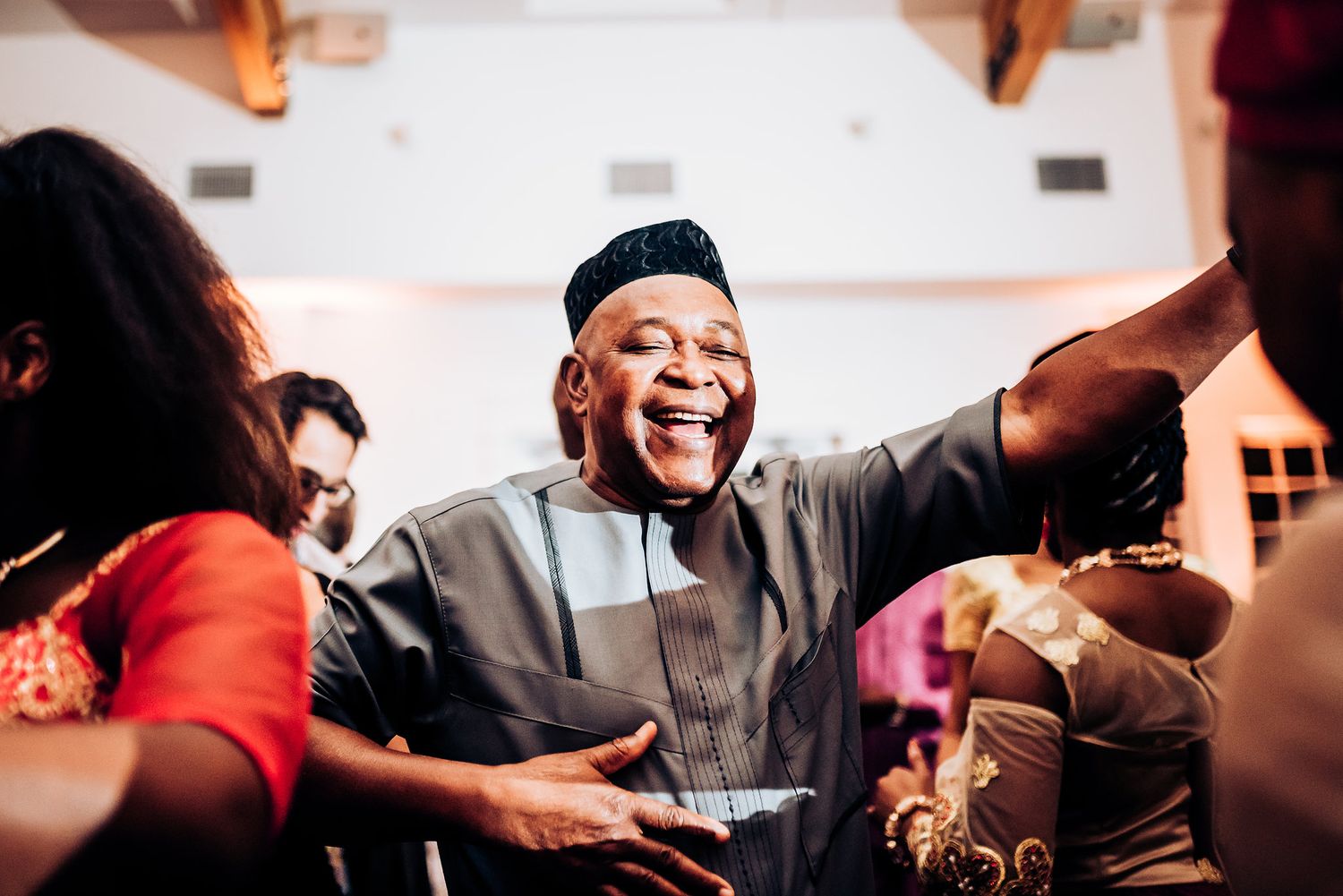 Guest in traditional attire smiles and dances during lively wedding celebration.