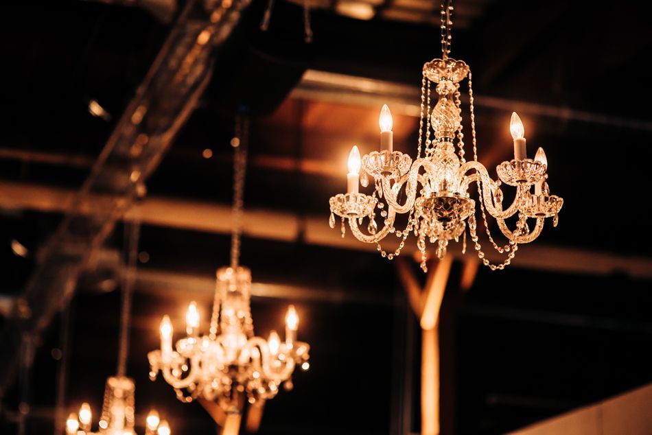 Crystal chandeliers hang from an industrial ceiling creating elegant ambient lighting.