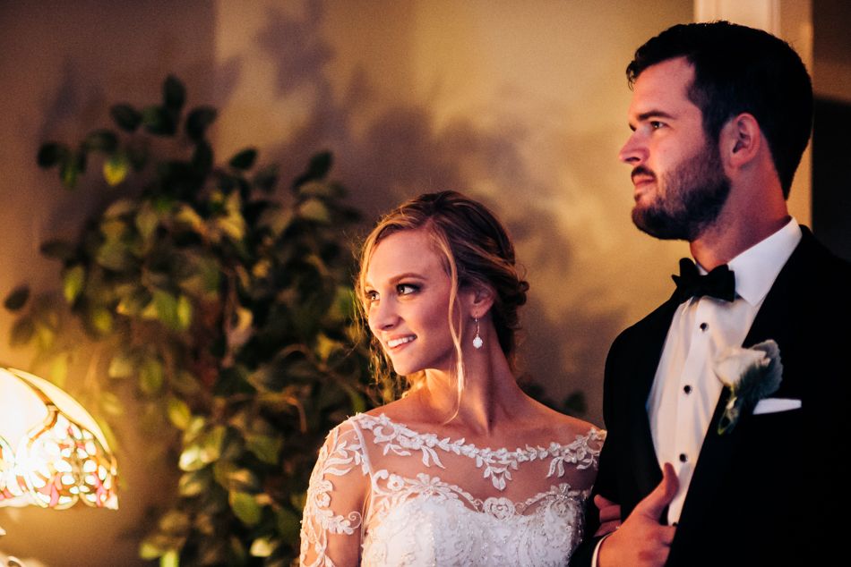 Couple shares intimate moment during wedding reception with decorative lighting and greenery.