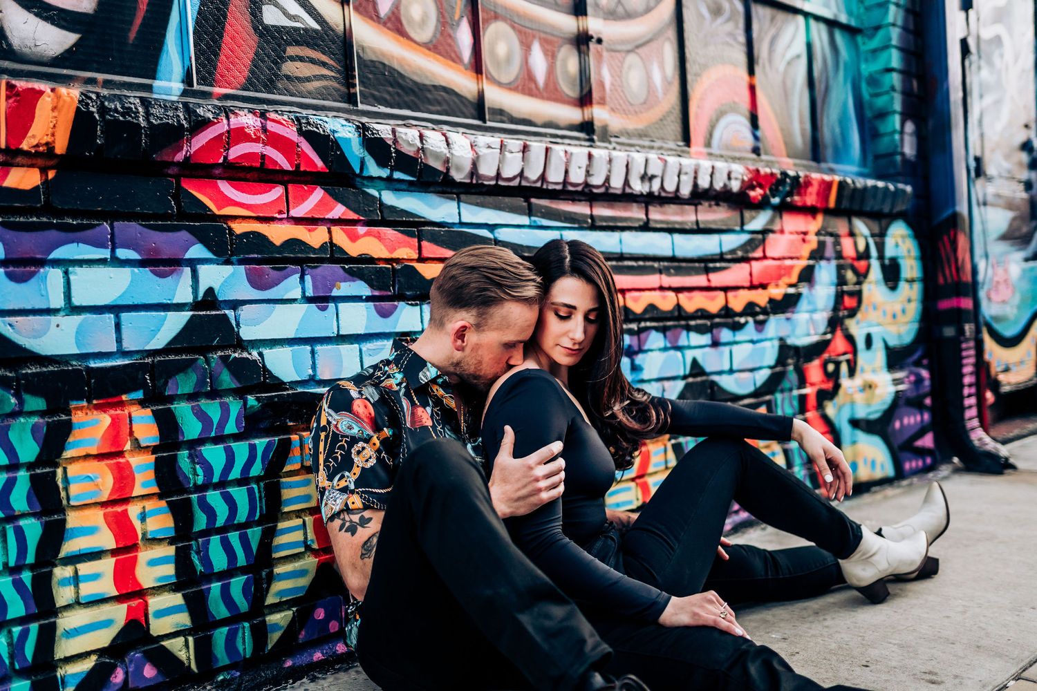 A couple sits together against colorful street art featuring bold lips and graffiti designs.